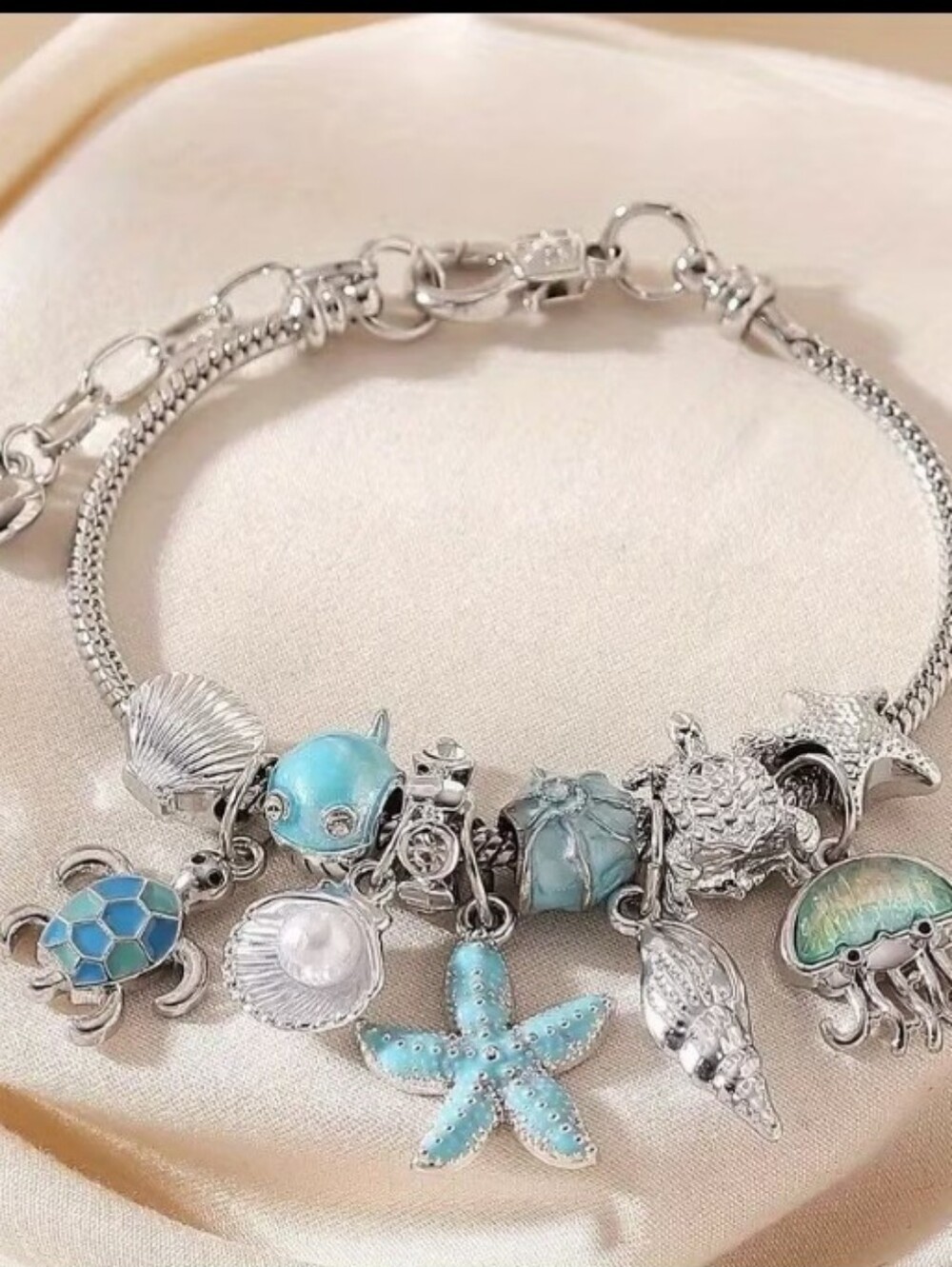 Elegant silver-tone charm bracelet featuring ocean-inspired charms. Turquoise an